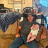 Johnny is registered to the contest to win money with this photo: baby, man, couch, living_room, cap, jeans, tshirt, blanket, pillow, person, kitchen, chair, window, light_fixture, indoor, family, casual, relaxed, home, seated