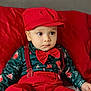 baby, child, toddler, red_clothing, bow_tie, suspenders, hat, face, person, indoor, cushion, red_cushion, sitting, cute, expression, hand, shoe, holiday_theme, patterned_shirt, portrait
