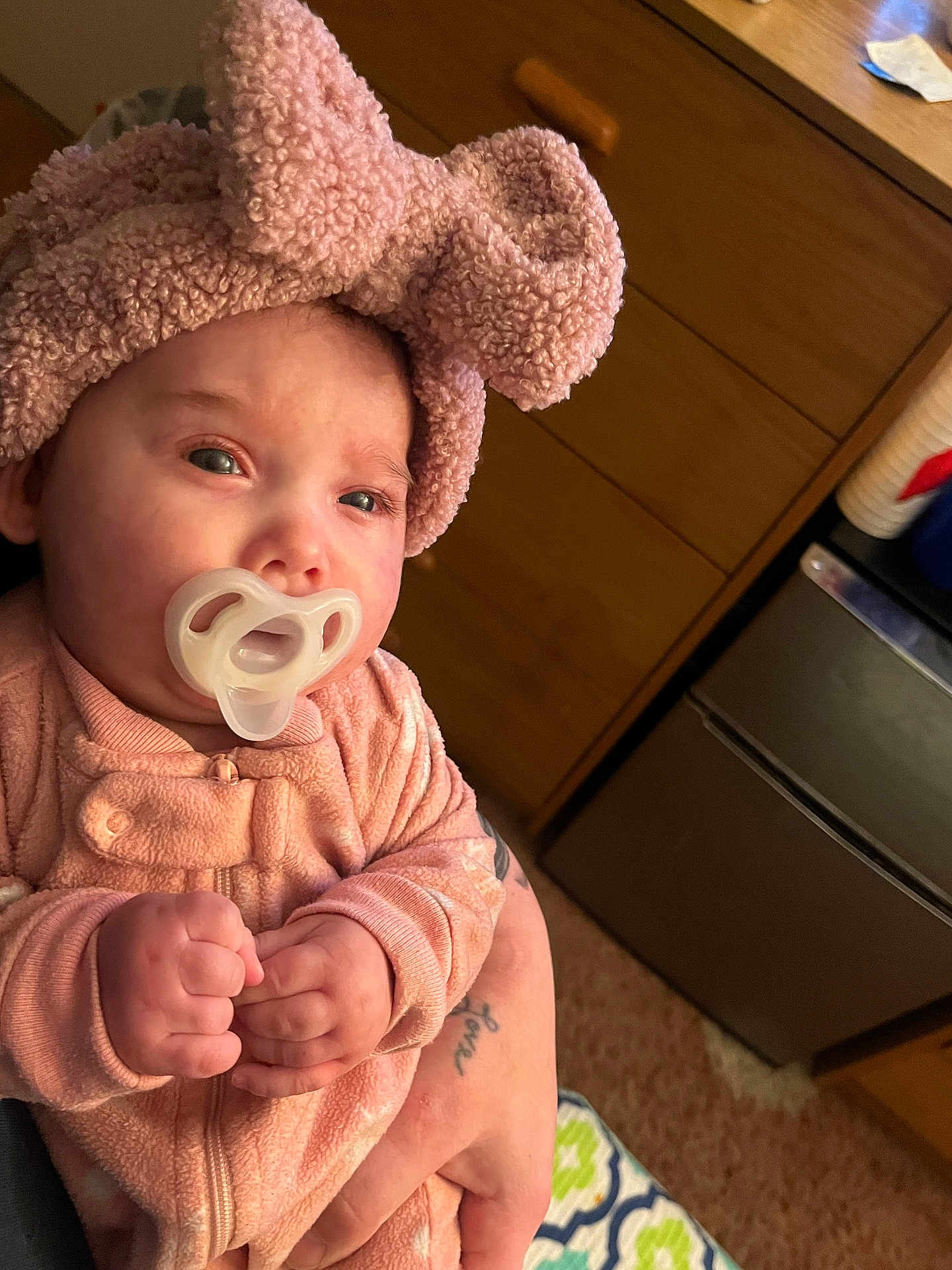 Kylee is registered to the contest to win money with this photo: baby, infant, pacifier, pink_clothing, headband, bow, fist, tattoo, hand, person, indoor, carpet, dresser, blanket, sleepwear, cute, child, soft_texture, warm_lighting, closeup