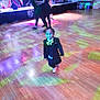 child, toddler, suit, bow_tie, dance_floor, party, disco_lights, hardwood_floor, stage, musicians, adults, dancing, formal_wear, colorful_lights, event, indoor, smile, single_child, spotlight, celebration
