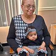 Maecii is registered to the contest to win money with this photo: elderly_woman, baby, indoor, smile, woman, child, seated, headband, glasses, patterned_clothing, black_and_white, affection, holding, window_blinds, chair, nail_polish, portrait, person, family, casual