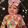 Stella is registered to the contest to win money with this photo: baby, child, bow, headband, onesie, colorful_clothing, floral_pattern, smile, face, cheeks, lying_down, quilt, stars, black_background, cute, infant, portrait, happy, indoors, person