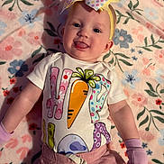 Stella joined the competition — help win amazing prizes! baby, child, infant, smile, tongue_out, headband, bow, shirt, carrot, clothing, blanket, floral_pattern, pink_gloves, pink_pants, lying_down, cute, happy, indoors, portrait, person