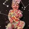 baby, child, smiling, onesie, headband, bow, patterned_clothing, star_pattern, quilt, constellation, black_background, colorful, happy, infant, lying_down, motion_blur, playful, cute, portrait, indoor