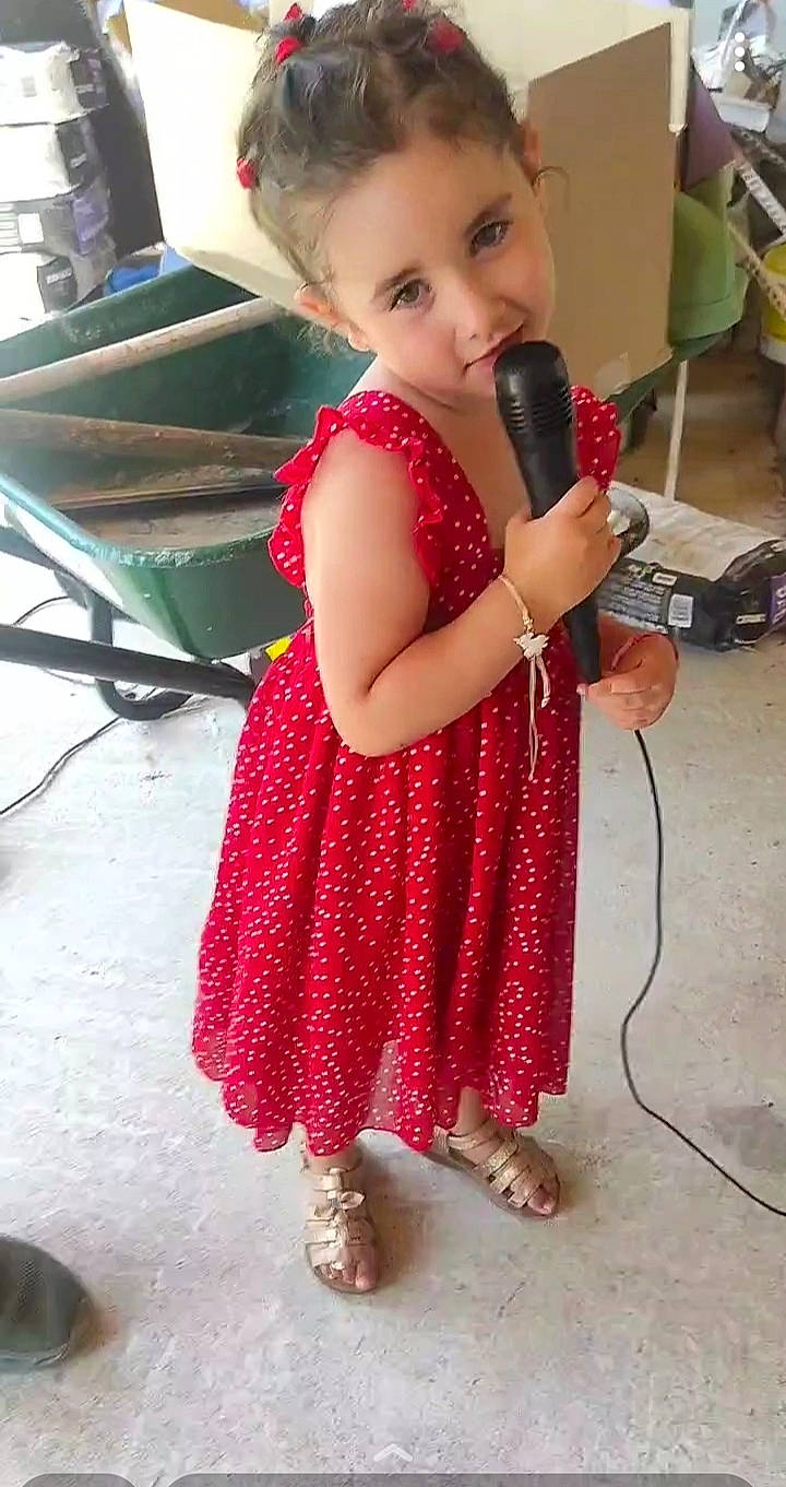 Carla participe au concours pour gagner de l'argent avec cette photo : audio_equipment, baby, baby_toddler_clothing, cart, child, dress, event, flooring, foot, fun, hair, happy, human_body, microphone, pattern, person, sandal, sitting, skin, toddler