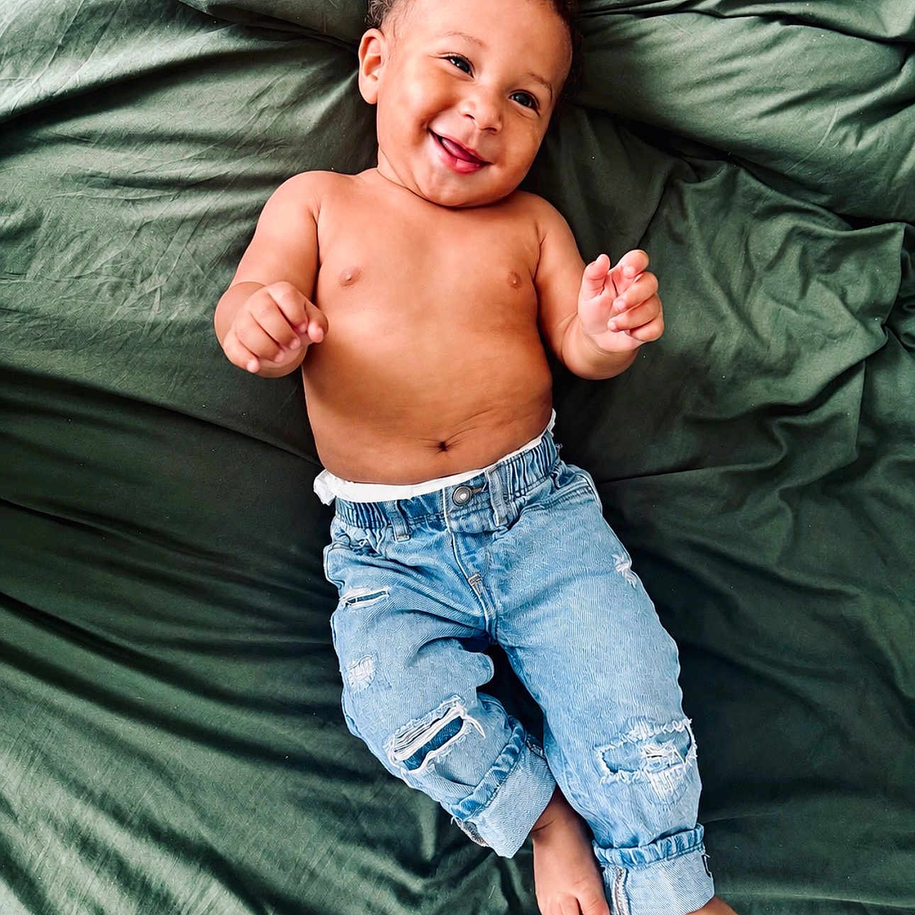 Brave joined the competition — help win amazing prizes! baby, child, infant, smiling, happy, portrait, lying_down, bed, bedding, green_sheets, denim, jeans, bare_chest, curly_hair, hands, feet, indoor, close_up, candid, fashion