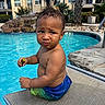 Brave is registered to the contest to win money with this photo: child, toddler, baby, pool, swimming_pool, poolside, lounge_chair, outdoor, portrait, curly_hair, smiling, serious_expression, blue_water, swimwear, tropical, palm_trees, apartment_building, sunlight, green_fruit, sitting
