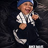 baby, child, infant, smiling, happy, portrait, indoor, sitting, sportswear, tracksuit, beanie, nike, clothing, black_and_white, couch, fabric, face, hands, fashion, text_overlay