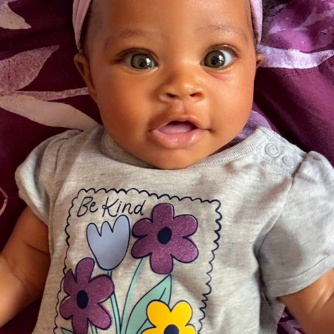 La-Zaria is registered to the contest to win money with this photo: baby, blanket, bow, child, clothing, cute, eyes, flowers, happy, headband, indoors, infant, ladybug, lying_down, pattern, portrait, purple, shirt, smiling, toddler