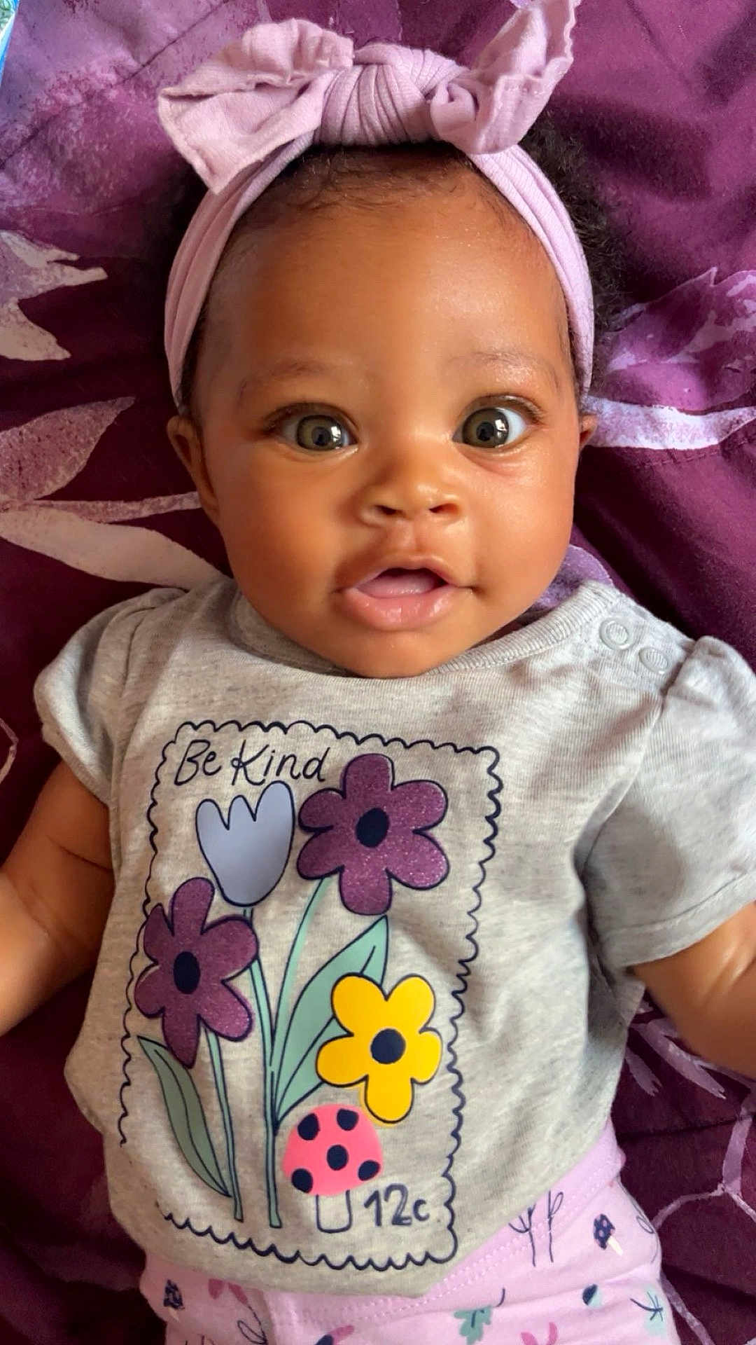 La-Zaria is registered to the contest to win money with this photo: baby, blanket, bow, child, clothing, cute, eyes, flowers, happy, headband, indoors, infant, ladybug, lying_down, pattern, portrait, purple, shirt, smiling, toddler