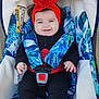 baby, infant, smiling, stroller, car_seat, headband, red_flower, harness, buckle, blue_pattern, clothing, cute, portrait, hands, eyes, blanket, outdoor, seat_padding, black_pants, red_socks