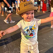 Adam participe au concours pour gagner de l'argent avec cette photo : toddler, child, hat, straw_hat, mickey_mouse, tshirt, shorts, smile, happy, arms_outstretched, outdoor, night, crowd, people, blurred_background, footwear, pavement, fun, joy, portrait
