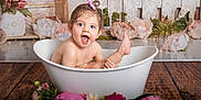 Melya a rejoint le concours — aidez-le/la à gagner de superbes lots ! baby, toddler, bathtub, white_tub, flowers, pink_bow, blue_eyes, splash, water_droplets, smile, surprised, studio_backdrop, wooden_floor, portrait, skin, happy, playful, indoors, rosy_cheeks, prop_decor
