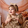 child, toddler, baby, headband, bow, dress, wicker_chair, portrait, smile, blue_eyes, hands, props, floral_backdrop, fabric, studio, rosy_cheeks, seated, clothing, fashion, cute