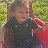 toddler, child, smiling, curly_hair, outdoor, sunlight, red_seat, grass, happy, black_clothing, baby, seatbelt, playtime, young_child, portrait, person, daylight, nature, cute, casual