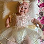 baby, smiling, flower_headband, lace_dress, infant, cute, lying_down, blanket, floral_pattern, happy, child, portrait, soft_lighting, indoors, toddler, young_child, person, head, arms, legs