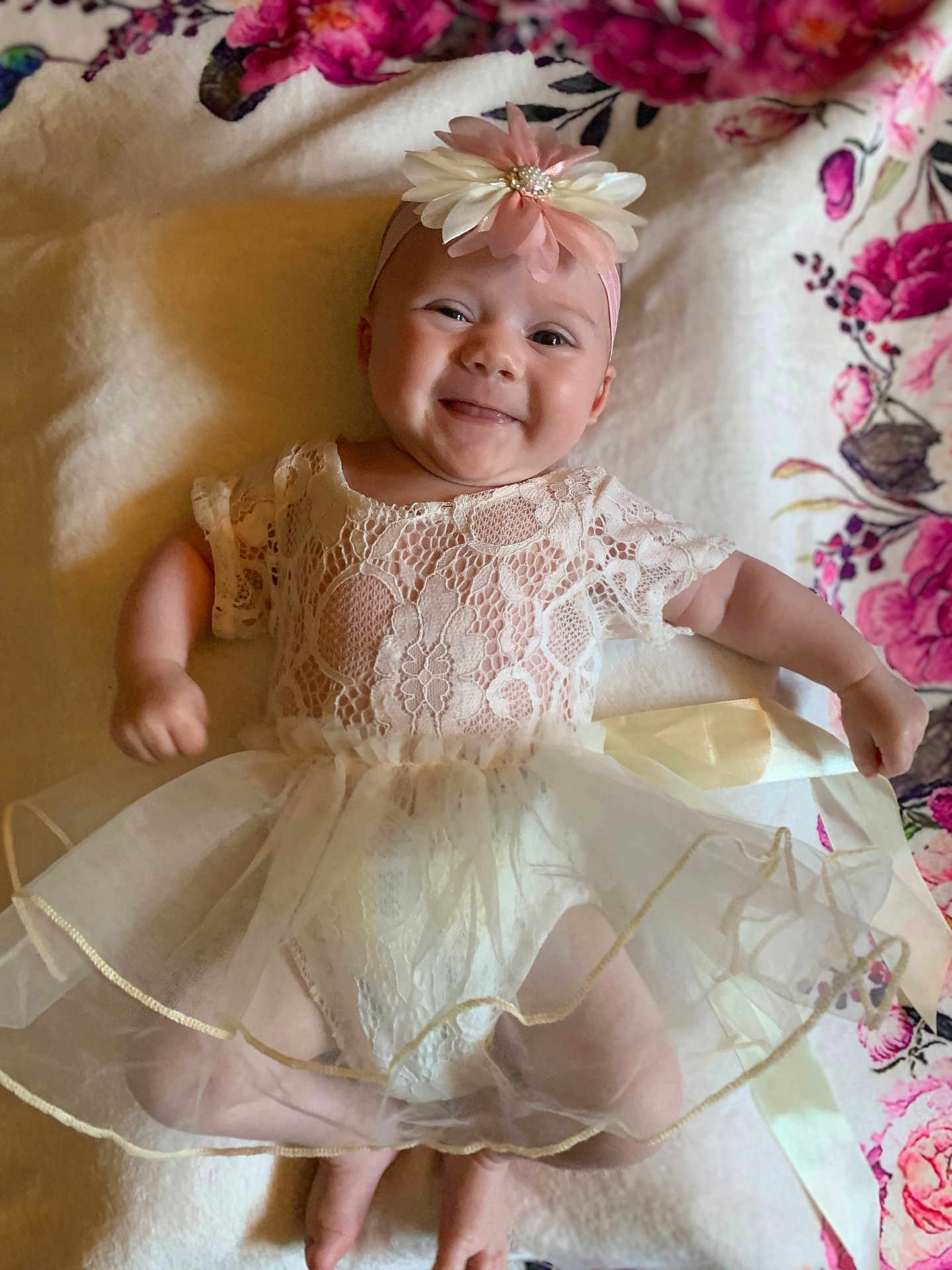 Merclynn is registered to the contest to win money with this photo: baby, smiling, flower_headband, lace_dress, infant, cute, lying_down, blanket, floral_pattern, happy, child, portrait, soft_lighting, indoors, toddler, young_child, person, head, arms, legs