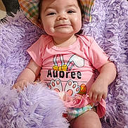 Aubree is registered to the contest to win money with this photo: baby, child, smile, hat, pink_clothing, fluffy_blanket, purple_blanket, infant, cute, portrait, happy, indoor, person, sitting, colorful, checkered_pattern, soft_texture, young_child, apparel, relaxed