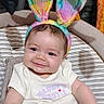 Aubree is registered to the contest to win money with this photo: baby, bunny_ears, colorful, cute, smile, infant, child, seat, cushion, striped, clothing, white_shirt, purple_pants, indoor, happy, face, person, headband, playful, adorable