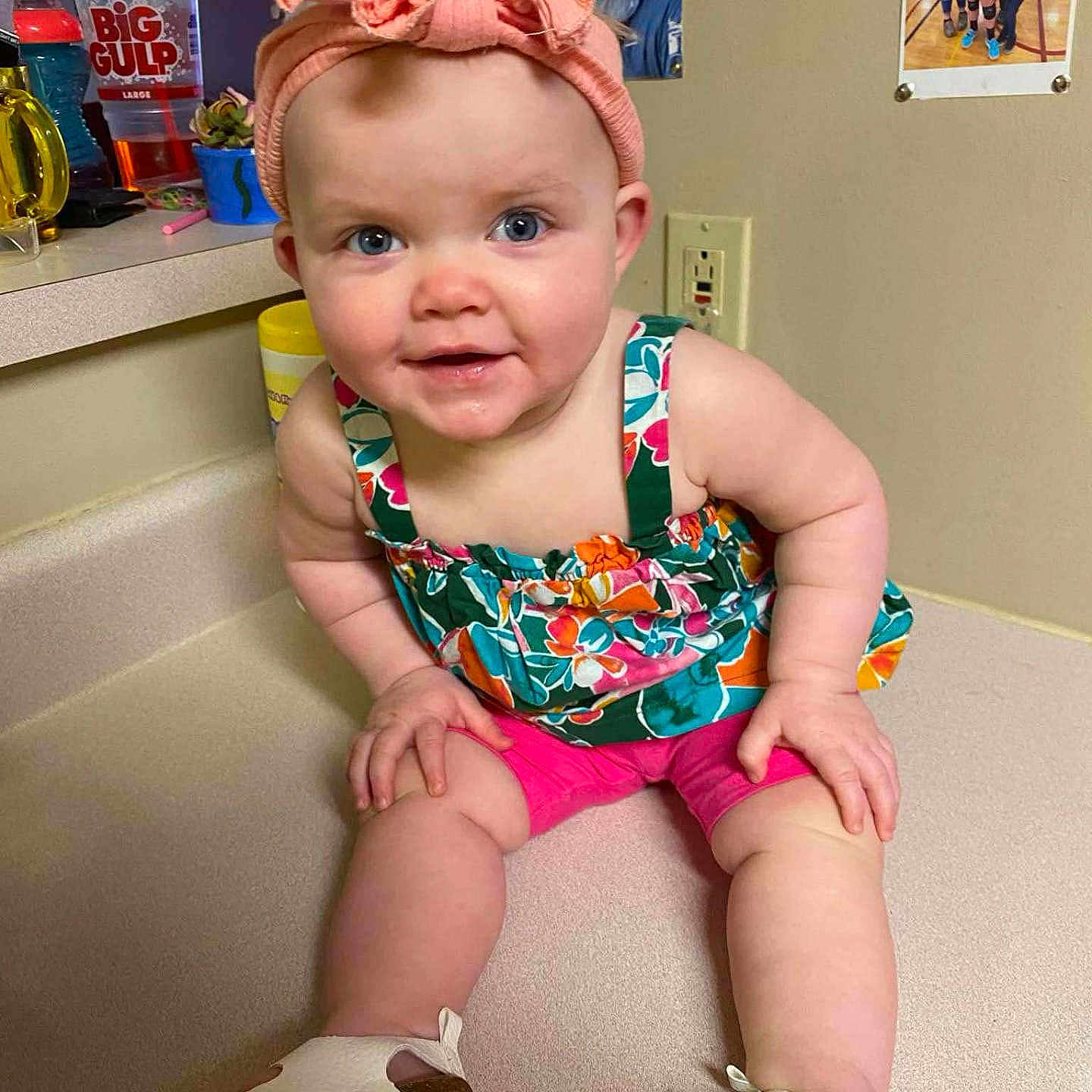 Amelia is registered to the contest to win money with this photo: baby, blue_eyes, casual, child, colorful_clothing, countertop, cute, drink_cup, family_photos, happy, headband, indoor, kitchen, person, pink, portrait, shoes, sitting, smiling, young_child