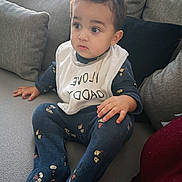 Wassîl participe au concours pour gagner de l'argent avec cette photo : toddler, child, baby, sitting, couch, bib, clothing, indoor, curious, portrait, person, home, furniture, patterned_clothing, cozy, young_child, cute, expression, face, casual