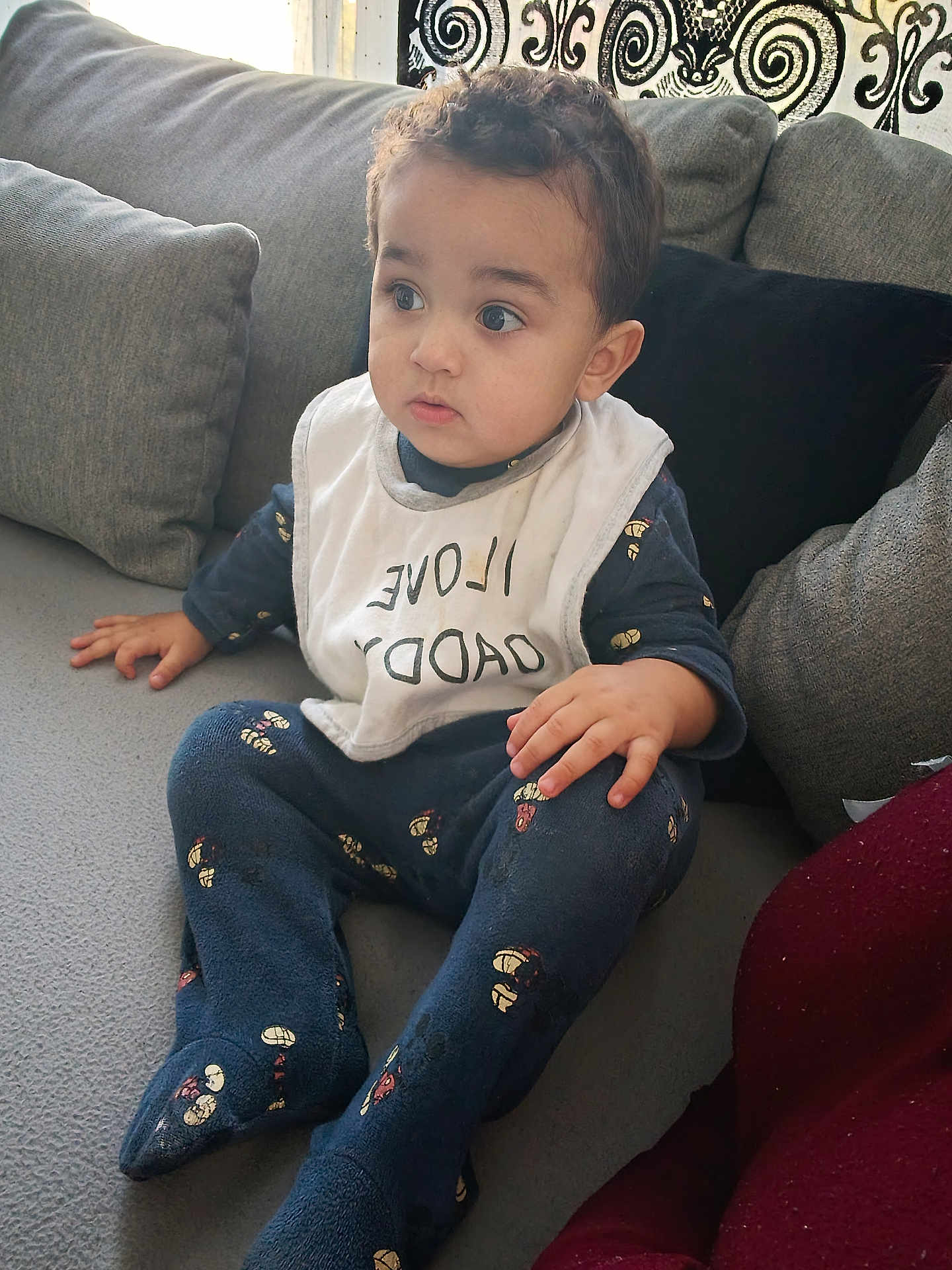Wassîl participe au concours pour gagner de l'argent avec cette photo : toddler, child, baby, sitting, couch, bib, clothing, indoor, curious, portrait, person, home, furniture, patterned_clothing, cozy, young_child, cute, expression, face, casual