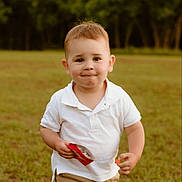 Kamden joined the competition — help win amazing prizes! toddler, child, boy, white_polo, khaki_shorts, outdoor, grass, snack, wrapper, smile, face, short_hair, daylight, nature, casual_clothing, young_child, running, playful, park, cute