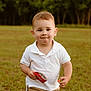 toddler, child, boy, white_polo, khaki_shorts, outdoor, grass, snack, wrapper, smile, face, short_hair, daylight, nature, casual_clothing, young_child, running, playful, park, cute