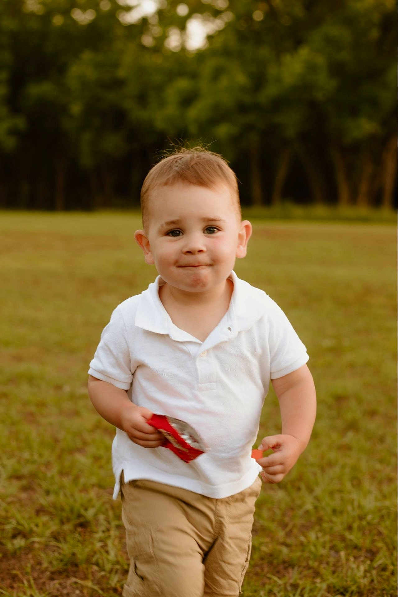 Kamden joined the competition — help win amazing prizes! toddler, child, boy, white_polo, khaki_shorts, outdoor, grass, snack, wrapper, smile, face, short_hair, daylight, nature, casual_clothing, young_child, running, playful, park, cute