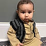 Ismail joined the competition — help win amazing prizes! baby, barefoot, beige_outfit, black_and_white, carpet, child, cute, floor, hand, head, indoor, infant, person, portrait, serious_expression, sitting, traditional_clothing, vest, wall, young