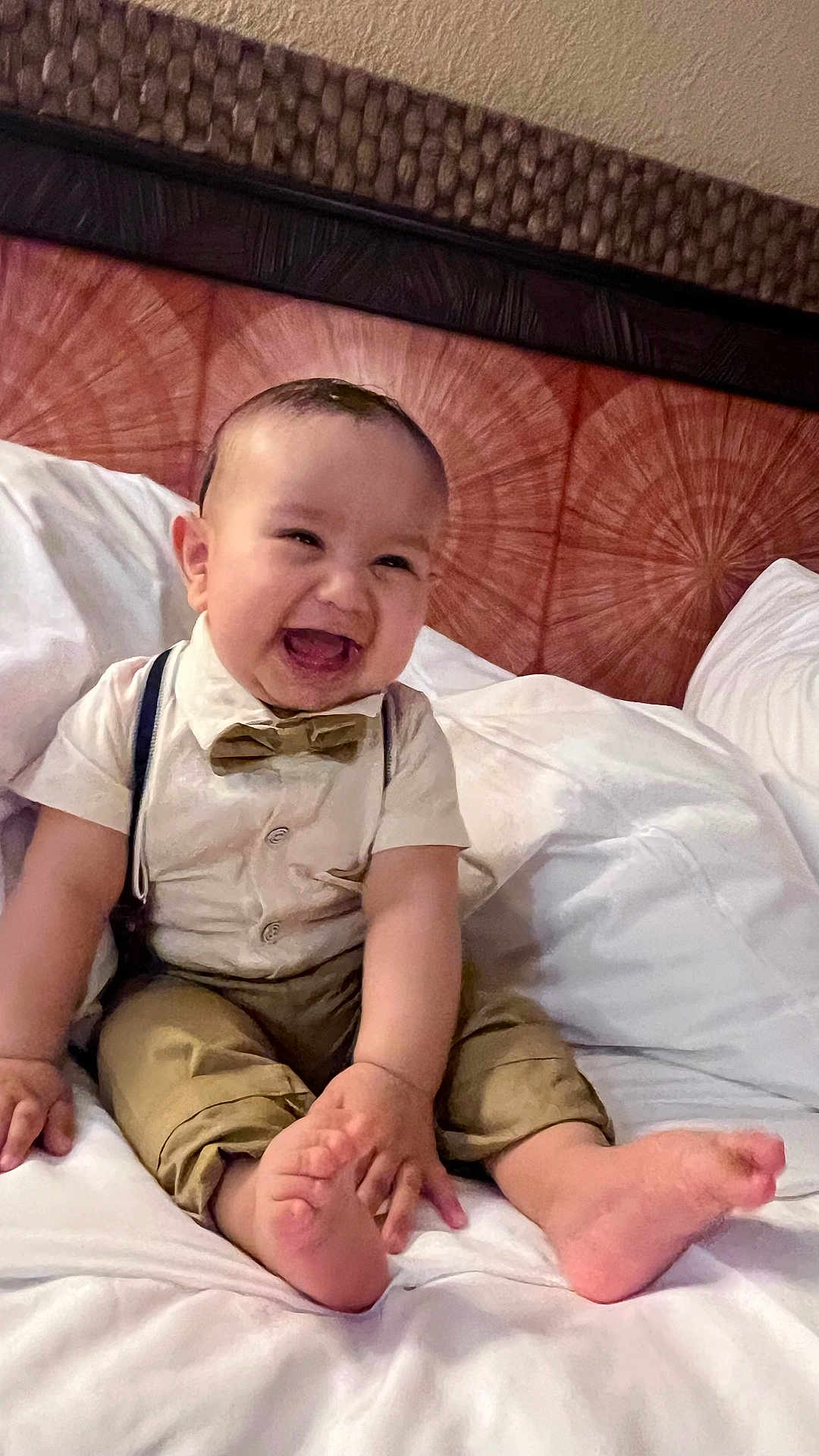 Ismail joined the competition — help win amazing prizes! baby, smiling, bow_tie, suspenders, bed, white_bed, happy, child, infant, cute, hands, feet, clothing, indoors, headboard, person, portrait, joyful, sitting, skin