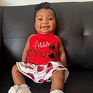 Genesis joined the competition — help win amazing prizes! baby, smiling, sitting, red_top, ladybug_print, skirt, black_headband, white_booties, leather_couch, indoor, child, cute, happy, portrait, infant, clothing, footwear, person, headwear, fashion
