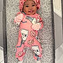 baby, infant, smiling, pink_onesie, bonnet, milk_print, cookie_print, crib, mattress, patterned_bedding, happy, tongue_out, lying_down, cute, child, soft_lighting, indoors, cozy, comfortable, playpen