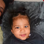 Néo participe au concours pour gagner de l'argent avec cette photo : toddler, child, face, smile, eyes, hair, pillow, black_clothing, portrait, indoors, cute, baby, person, lying_down, soft_texture, home, curious, head, young_child, closeup