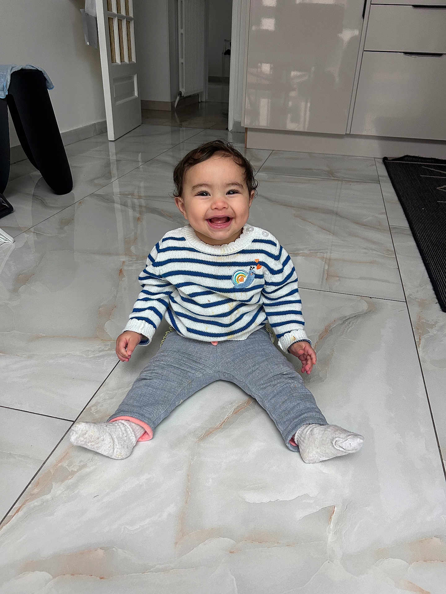 Janah participe au concours pour gagner de l'argent avec cette photo : toddler, child, smiling, indoor, floor, tile, sweater, pants, socks, happy, person, baby, home, door, cabinet, curly_hair, seated, cute, young, playful