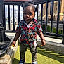toddler, child, portrait, outdoor, sunny, grass, urban, railing, building, pigtails, shirt, sneakers, curious, standing, daylight, person, fashion, casual, young_child, expression