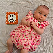 Hadley is registered to the contest to win money with this photo: baby, infant, three_months, milestone_card, floral_dress, pink, strawberry, blanket, lying_down, hands, feet, blue_eyes, portrait, smile, cute, fabric, pattern, bedroom, soft_texture, photo