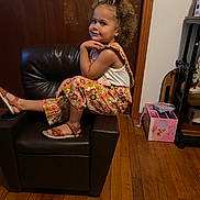 Kaleigha is registered to the contest to win money with this photo: child, curly_hair, bow, chair, leather_chair, floral_pants, white_tank_top, sandals, wooden_floor, indoor, toy_box, pink_box, smile, posing, furniture, person, home, casual_clothing, happy, cute