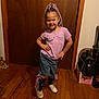 Kaleigha is registered to the contest to win money with this photo: child, smiling, posing, indoor, wooden_floor, door, pink_shirt, denim_shorts, white_shoes, colorful_braids, necklace, black_socks, decorative_legwear, wooden_door, bag, toy_box, floor, happy, person, casual_clothing