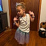 child, girl, princess, tiara, necklace, bracelet, earrings, skirt, white_top, wooden_floor, wooden_door, indoor, pose, playful, jewelry, purple, home, person, smile, fashion