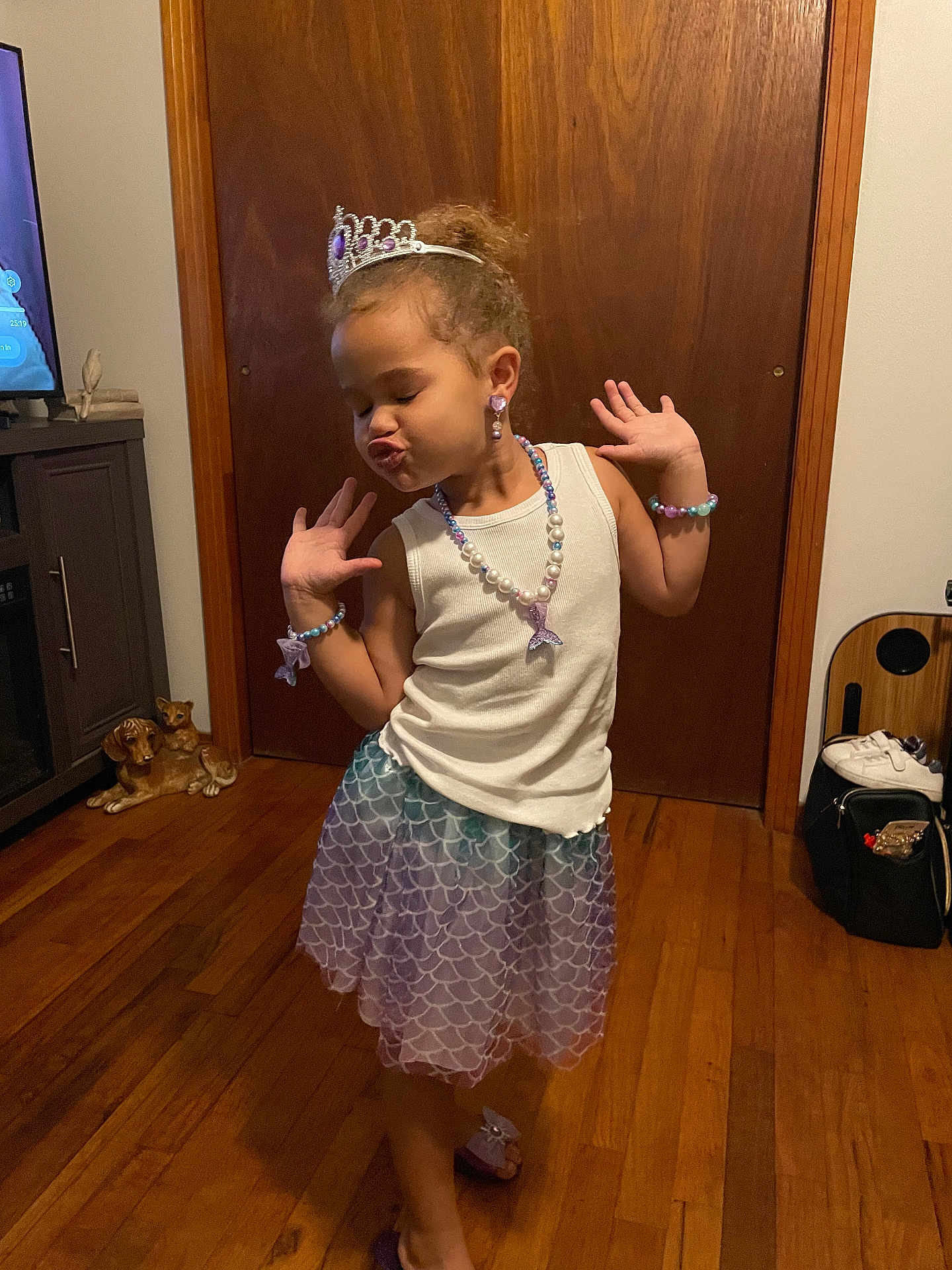 Kaleigha is registered to the contest to win money with this photo: child, girl, princess, tiara, necklace, bracelet, earrings, skirt, white_top, wooden_floor, wooden_door, indoor, pose, playful, jewelry, purple, home, person, smile, fashion