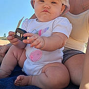 Peyton is registered to the contest to win money with this photo: baby, child, outdoor, sunlight, hat, onesie, car_key, towel, person, skin, expression, hand, foot, summer, casual, sitting, adult, nature, daytime, closeup