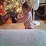 toddler, child, christmas_tree, lights, indoor, floor, fan, rocking_chair, curtains, book, onesie, patterned_clothing, baby, holiday, decorations, home, furniture, person, standing, cozy