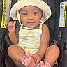 baby, child, car_seat, hat, romper, smile, feet, toes, sitting, infant, cute, happy, indoors, safety, warning_label, skin, clothing, headwear, person, portrait