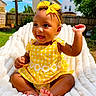Isla joined the competition — help win amazing prizes! baby, blanket, bow, child, curly_hair, face, fence, grass, happy, headband, house, outdoor, playful, portrait, sitting, smiling, summer, sunlight, toes, yellow_dress