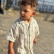 Mark participe au concours pour gagner de l'argent avec cette photo : child, boy, curly_hair, striped_shirt, short_sleeves, pavement, outdoor, daylight, portrait, standing, casual_clothing, background_blur, fence, curious, person, young_child, summer, sunlight, side_view, urban_outdoor