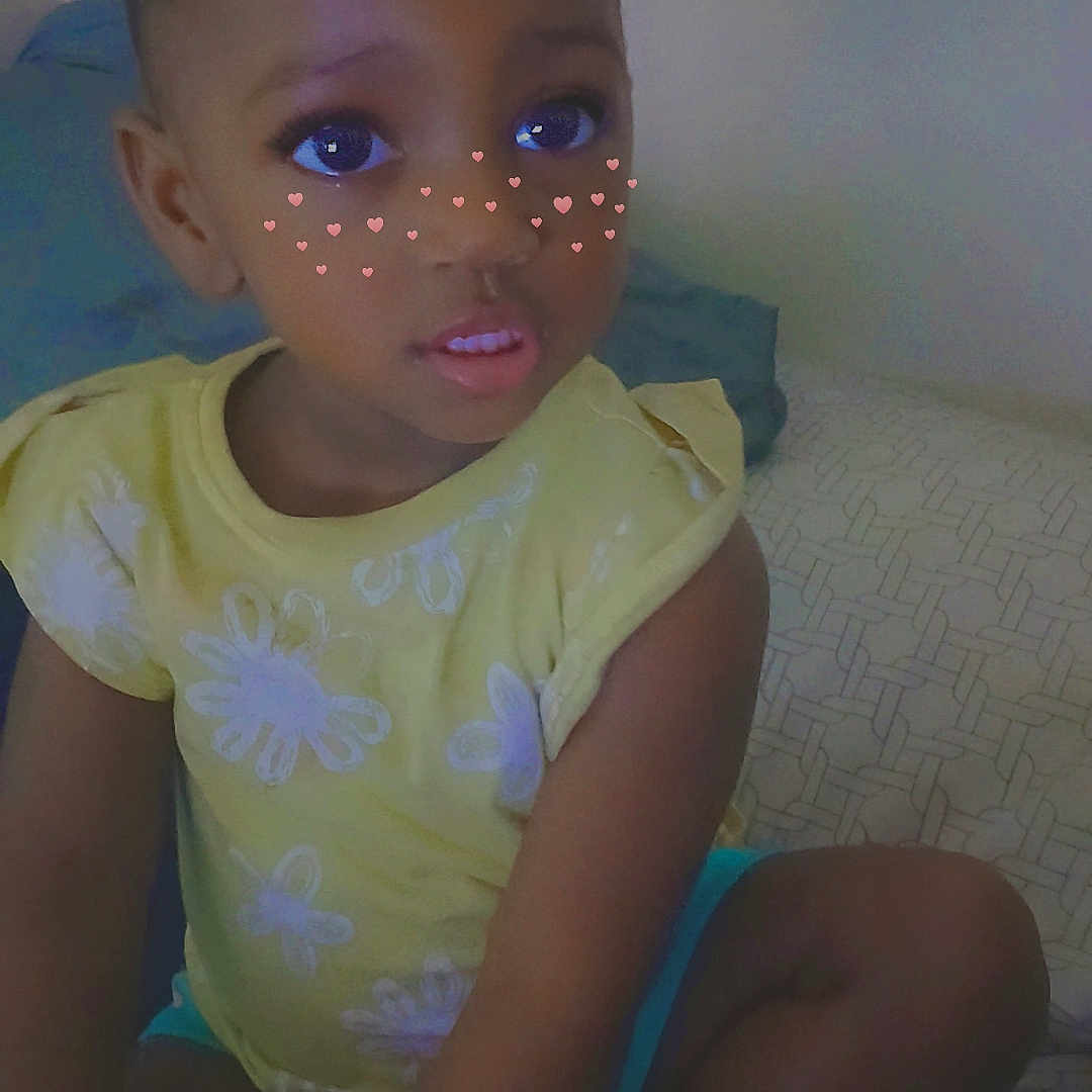 Jay'Anah is registered to the contest to win money with this photo: baby, bodypart, clothing, couch, face, finger, furniture, hand, happy, hat, head, indoors, person, photography, portrait, shorts, sitting, smile, t_shirt, toy