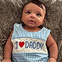 baby, infant, child, blue_clothing, checkered_pattern, embroidered_text, heart_symbol, daddy_message, plush_blanket, soft_texture, cute, chubby_cheeks, lying_down, small_hands, curious_expression, natural_light, portrait, indoors, comfortable, smiling