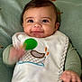 Myles is registered to the contest to win money with this photo: baby, child, face, smile, bib, drool, hand, green_clothing, knit_blanket, cute, infant, portrait, indoors, happy, young_child, closeup, sitting, soft_texture, baby_garment, waving