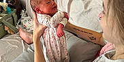 Eloise joined the competition — help win amazing prizes! baby, newborn, woman, holding, indoor, couch, pillow, onesie, floral, smile, person, tattoo, arm, face, home, casual, comfort, infant, bonding, relaxation
